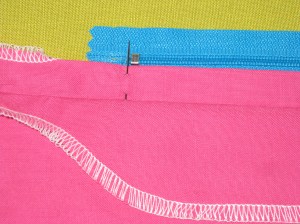 Position zip (coils up) under the folded back seam allowance - align the stop to the marked position.