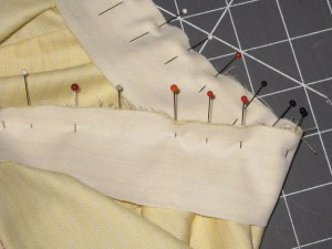 Neckline edge sandwiched between the collar stand pieces and pinned in place. Pinning at right angles to the seam keeps everything in place well when stitching curves.