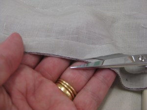 Resting fabric across your hand, carefully cut fabric right next to the stitching.